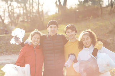 Smiling male and female volunteers with plastic garbage standing in park