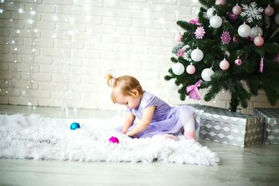 Baby girl sitting on rug by christmas tree