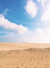 People walking on sand against cloudy sky