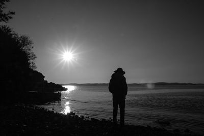 Silhouette man standing at sea shore against sky during sunset