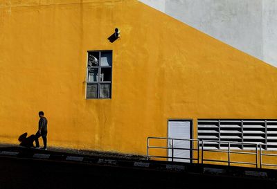 Man walking by yellow building wall in city during sunny day