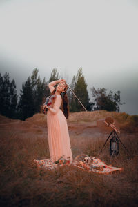 Woman standing by tree on field against sky