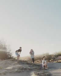 Mother standing with children at beach against clear sky