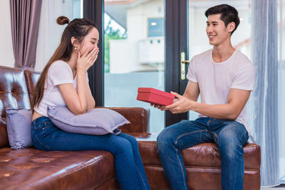 Boyfriend giving gift to girlfriend while sitting on sofa at home