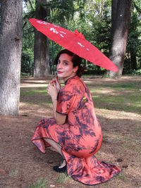 Young woman sitting on red umbrella in rain