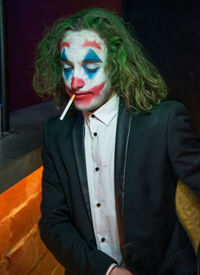 Man wearing clown make-up smoking cigarette while sitting indoors