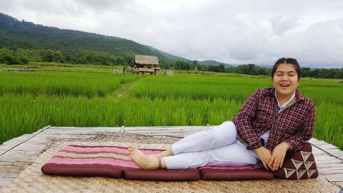 Portrait of happy young woman lying on mattress by agricultural field