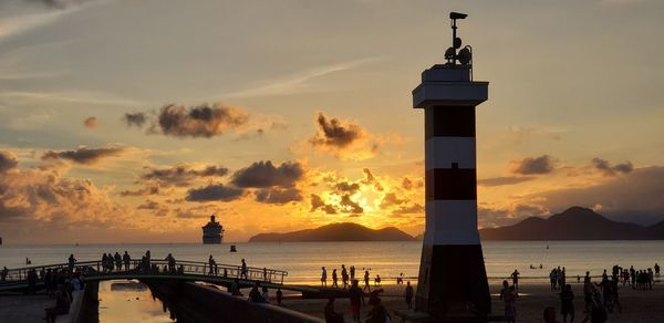 Lighthouse by sea against sky during sunset