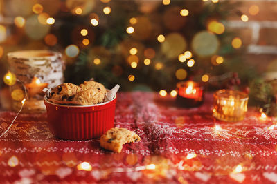 Red festive bowl full with christmas cookies, blurred christmas fir tree lights