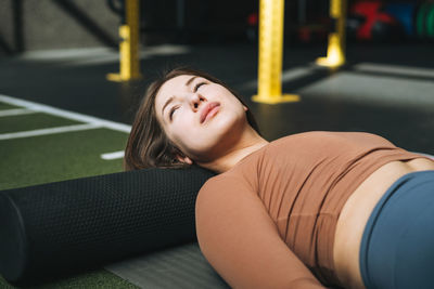 Young brunette woman doing stretching pilates on the massage roll in fitness club gym