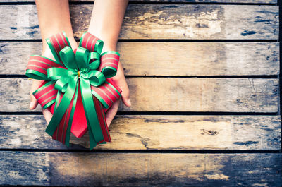 Directly above shot of cropped hands holding gift box at wooden table