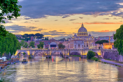 Arch bridge over river by buildings against sky during sunset