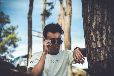 Portrait of young man standing by tree trunk