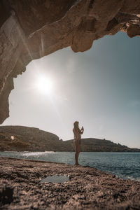 Man standing on rock by sea against sky