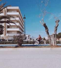 Man riding bicycle on road by buildings against sky