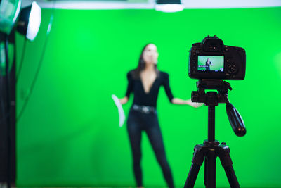 Full body of female host reading news on paper document while recording program for social media against chromakey screen