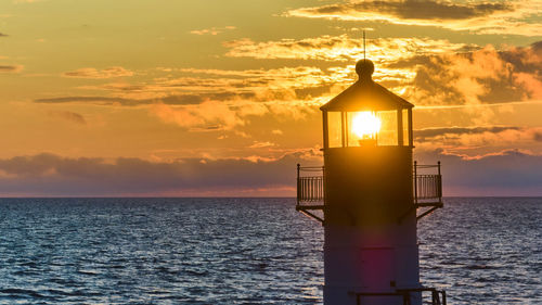 Lighthouse by sea against sky during sunset