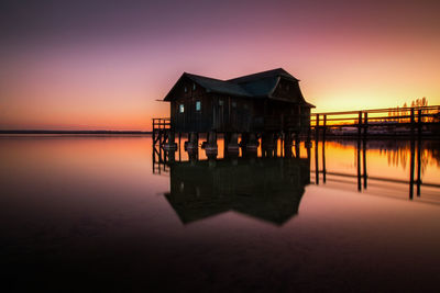 Wooden house on sea against sky during sunset