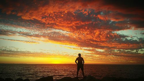 Silhouette man standing on beach against orange sky