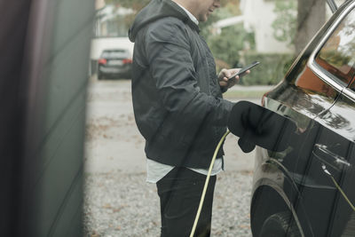 Mid adult man with electric car at charging station seen through glass