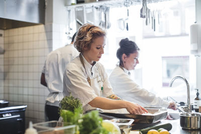 Female chefs preparing food on counter by colleagues in kitchen at restaurant