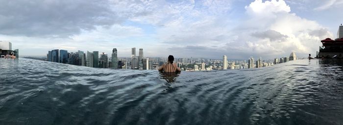 Rear view of woman in infinity pool against buildings in city