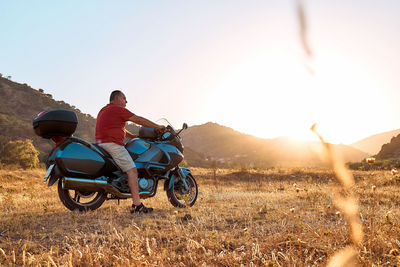 On the road.tourist man traveling on motorcycle, looking through binoculars at mountains in sunset