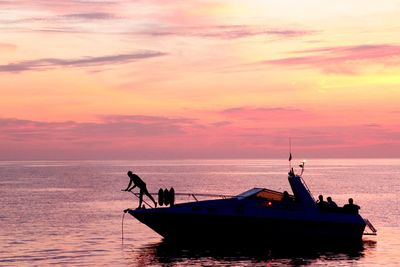 Silhouette man sailing boat in sea during sunset