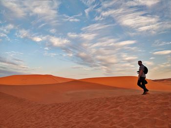 Man walking at desert against sky during sunset