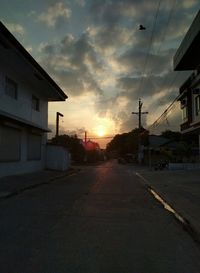 Road by buildings against cloudy sky