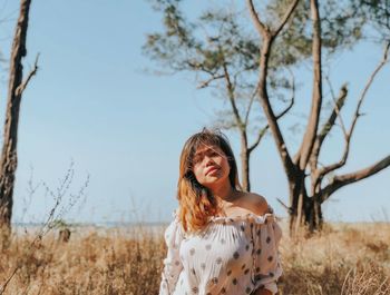 Portrait of young woman standing on field against clear sky