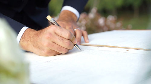 Midsection of bridegroom signing on book at wedding ceremony