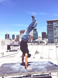 Full length of man doing handstand at building terrace on sunny day