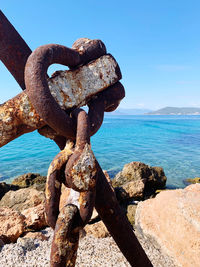 Close-up of rusty chain on rock by sea against sky