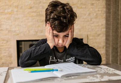 Cheerful and funny schoolboy solves  homework emotionally. thinks about how to solve math examples 