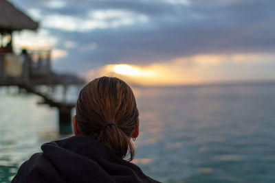 Rear view of woman by sea against sky during sunset