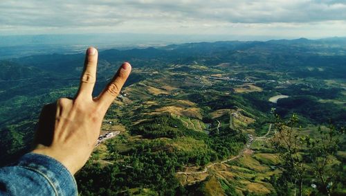 Cropped hand gesturing peace sign against landscape