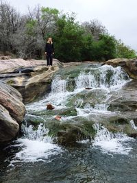 Mid distance view of woman standing on rocks at waterfall