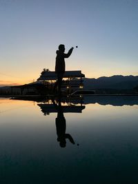 Silhouette man standing by lake against sky during sunset