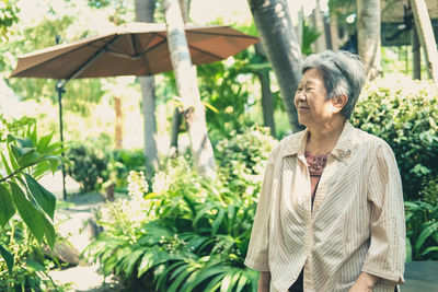 Smiling woman looking away while standing by plants