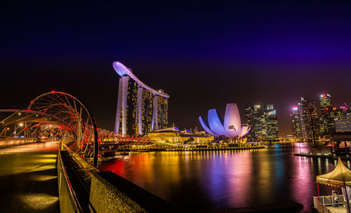 Illuminated city by river against sky at night