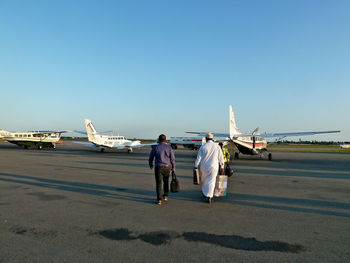 Rear view of people walking at airport runway against clear sky