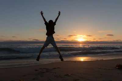 Silhouette boy jumping at beach against sky during sunset