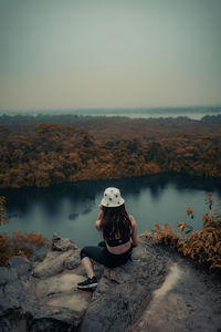 Man sitting on rock against sky