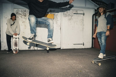 Male skater with skateboard jumping by friends on street