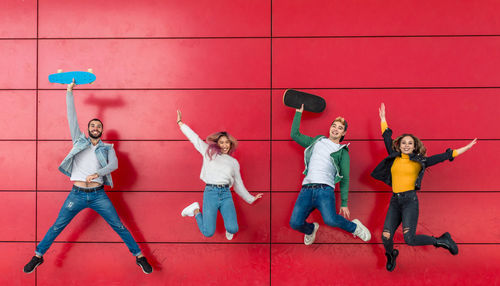 Full length of cheerful friends jumping against red wall