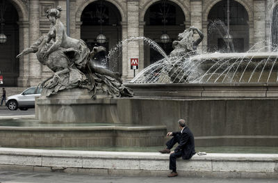 Man sitting by fountain at historic building