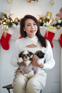 Beautiful woman in white dress hold two shih tzu puppies at home.
