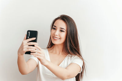 Portrait of smiling young woman using smart phone against white background