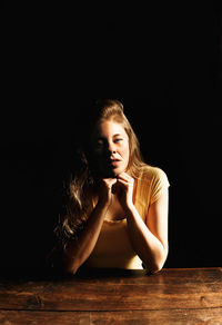 Portrait of woman sitting against black background